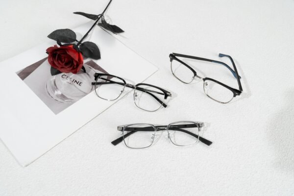 Modern eyewear arrangement with a red rose and stylish magazine backdrop.