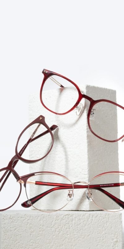 Stylish red and brown eyewear resting on white textured blocks in a minimal studio setup.